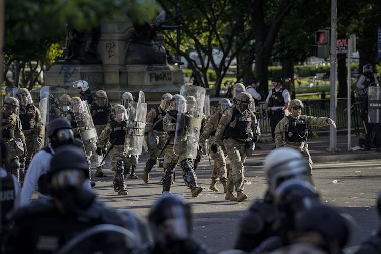 image - The Deeping People in military uniforms walk into an open paved area.